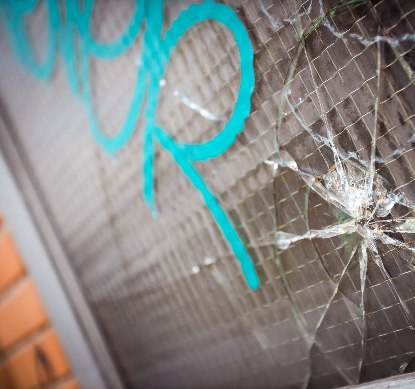 Bullet hole and cracks in a reinforced window with gang graffiti